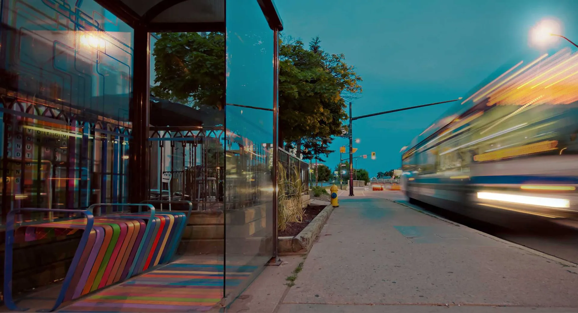 A city bus speeding past a colourful shelter at dusk