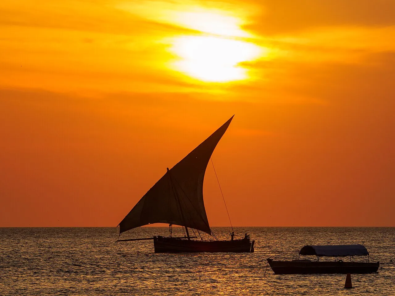 A dhow sailing boat silhouetted against an orange sunset